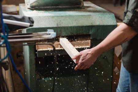 partial view of woodworker sawing plank in thickness planerの写真素材