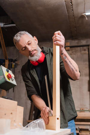 tattooed carpenter checking wooden plank in woodwork studioの写真素材