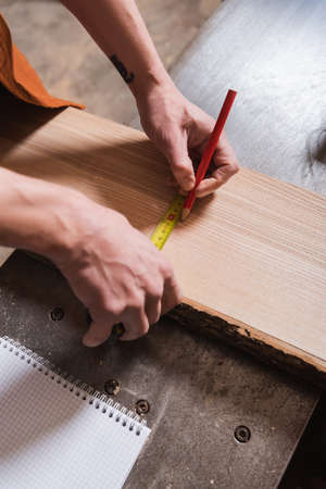 partial view of furniture designer with tape measure and pencil measuring board in workshopの写真素材