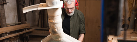 bearded carpenter in goggles working near blurred ventilation hood, banner