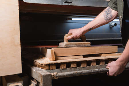 cropped view of tattooed carpenter polishing timber on sander machineの写真素材
