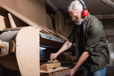 bearded woodworker polishing board in sander machineの写真素材