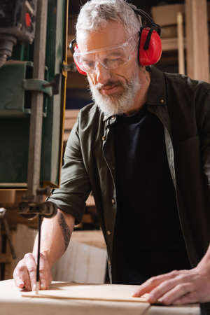 bearded carpenter in goggles cutting timber with band sawの写真素材