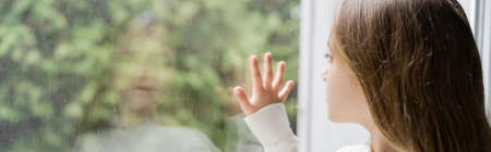 girl looking through window and touching glass with raindrops, bannerの写真素材