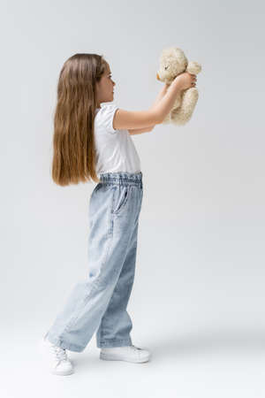 full length of girl in jeans holding teddy bear on greyの写真素材