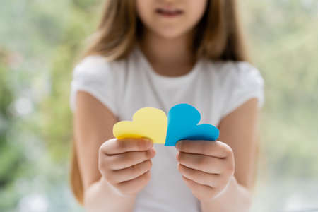 partial view of blurred girl holding blue and yellow paper heartsの写真素材