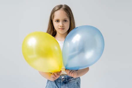 ukrainian girl holding blue and yellow balloons while looking at camera isolated on greyの写真素材