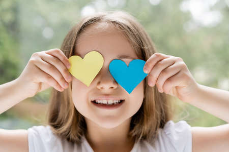 cheerful ukrainian girl obscuring face with blue and yellow paper heartsの写真素材