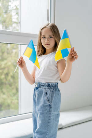 patriotic girl with small ukrainian flags standing near window and looking at cameraの写真素材