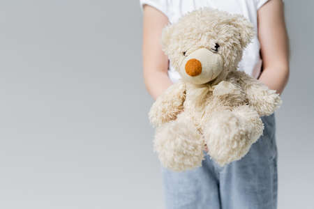 partial view of blurred girl holding teddy bear isolated on grey