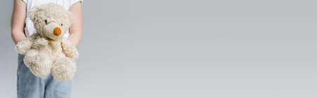 partial view of child holding teddy bear isolated on grey with copy space, bannerの写真素材