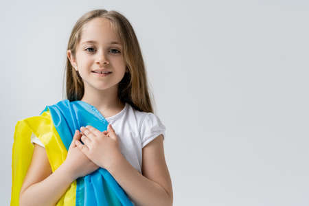 smiling girl with ukrainian national flag touching heart isolated on grey