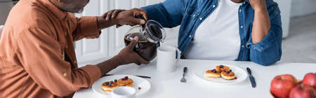 cropped view of senior african american man pouring coffee to wife during breakfast, bannerの写真素材