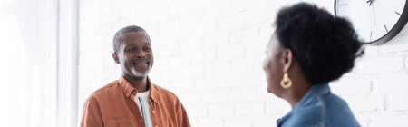 cheerful senior african american couple looking at each other in kitchen, banner