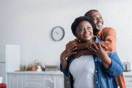 happy and senior african american man embracing smiling wife