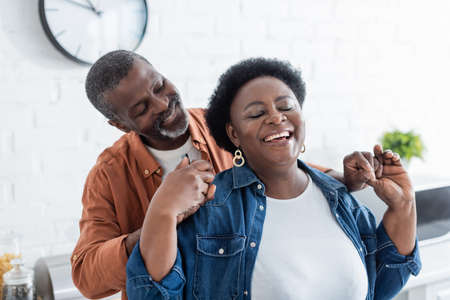 happy senior african american man holding hands of smiling wife with closed eyesの写真素材