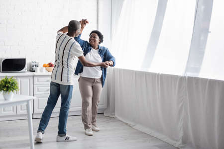 full length of cheerful senior african american couple dancing in kitchen