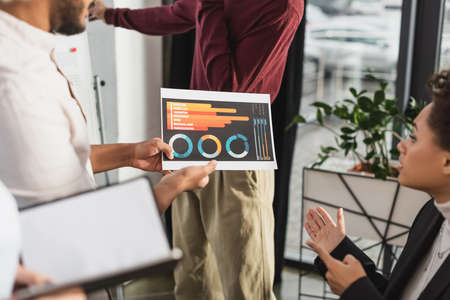 African american businesswoman pointing at paper with charts near colleagues in office