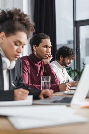 Focused african american businessman writing on notebook near interracial colleagues in office