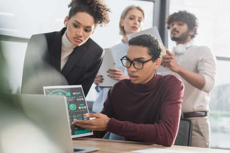 African american businessman pointing at paper during video call on laptop near blurred multiethnic colleagues in officeの写真素材