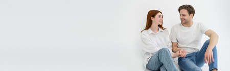 Positive young couple holding hands while sitting on white background, banner