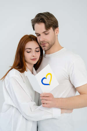 Man holding card with blue and yellow heart sign near girlfriend isolated on whiteの写真素材