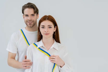 Young woman holding blue and yellow ribbon near smiling boyfriend isolated on white