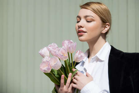 pretty blonde woman holding white tulips near blurred grey wallの写真素材