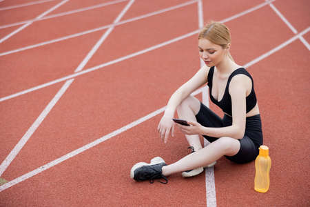 pretty woman in black sportswear sitting on stadium with mobile phone