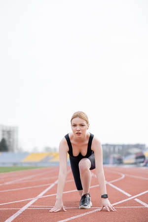 young sportive woman standing in low start position and looking at camera
