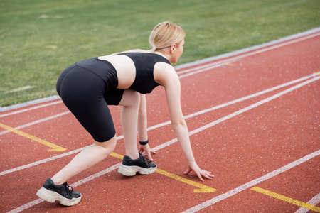 full length view of woman in black sportswear standing in low start position on stadiumの写真素材