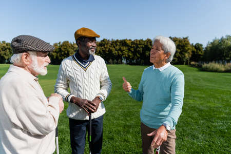 senior asian man gesturing and talking with multiethnic friends on golf fieldの写真素材