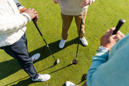 high angle view of interracial senior friends standing with golf clubs on lawnの写真素材
