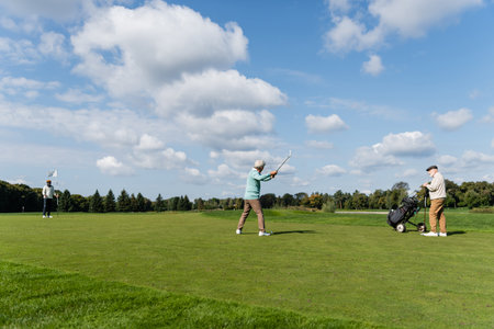 senior asian man playing golf near friends with flag stick and golf cartの写真素材