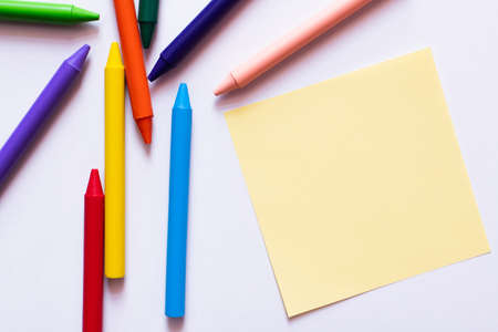 top view of colorful crayons near yellow paper note on white