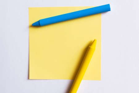 top view of blue and yellow crayons near paper note isolated on white