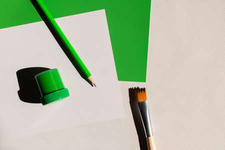 top view of paintbrush, pencil and jar with paint near white and green papers on textured background