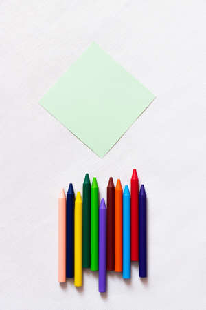top view of colorful crayons near empty paper note on textured white background