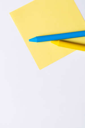top view of blue and yellow crayons on paper note isolated on white