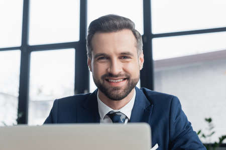 portrait of happy bearded businessman looking at camera on blurred foreground