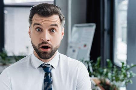 shocked economist with open mouth looking at camera in blurred officeの写真素材