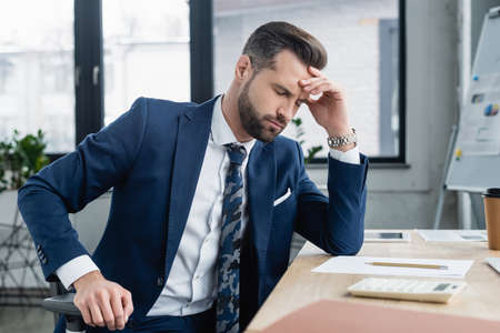 exhausted accountant sitting with closed eyes near blurred calculator on deskの写真素材