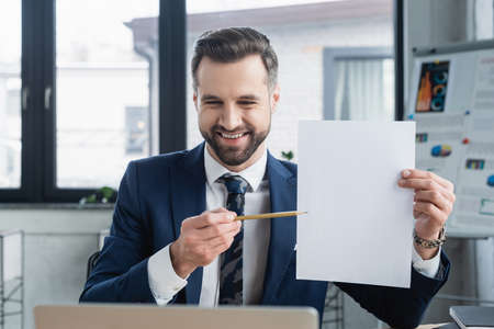 smiling economist pointing with pencil at empty paper in officeの写真素材