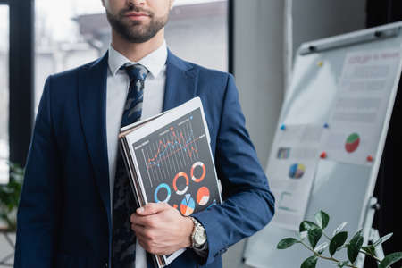 cropped view of economist in blazer holding folders and infographics