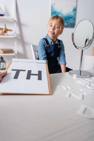 Speech therapist holding clipboard with letters near blurred pupil and mirror in consulting roomの写真素材