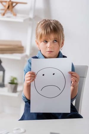 Skeptical kid holding paper with smile in classroom