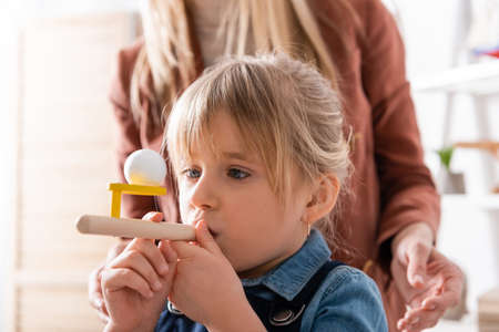 Kid using respiratory muscle trainer during lesson near logopedist in classroom