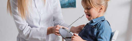 Logopedist in white coat holding tool near child with mirror in classroom, bannerの写真素材