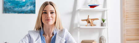 Logopedist in white coat looking at camera in consulting room, bannerの写真素材
