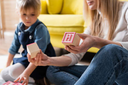 Wooden block with letter in hand of blurred speech therapist near child in consulting room